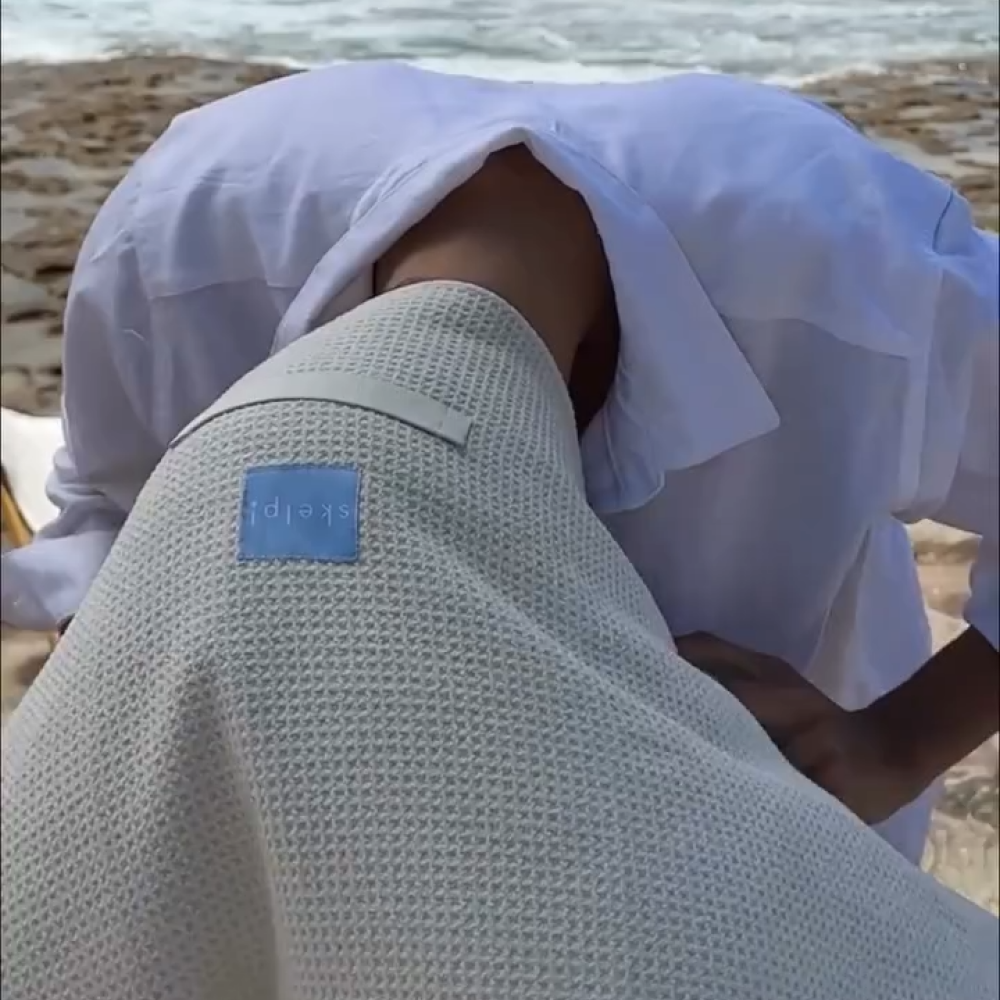 woman at beach using skelp! Microfibre Towel to quickly dry and protect her hair after swimming at the beach.