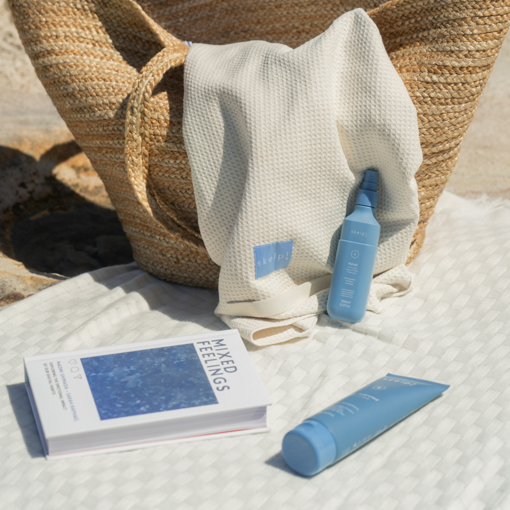skelp best selling haircare product hair mask and all in one treatment sitting on towel with book, woven basket at the beach