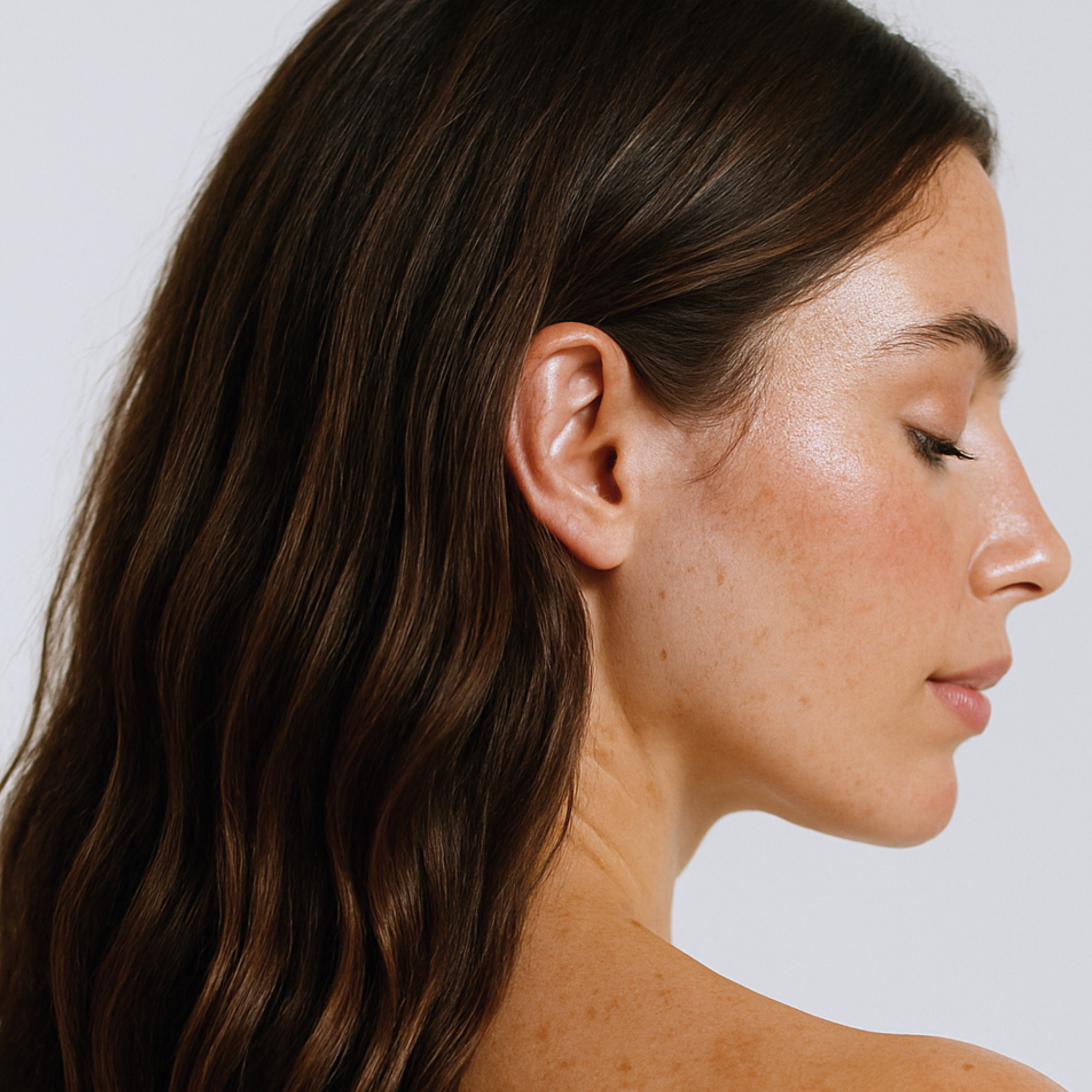 Side profile of a woman with wavy hair on a plain background
