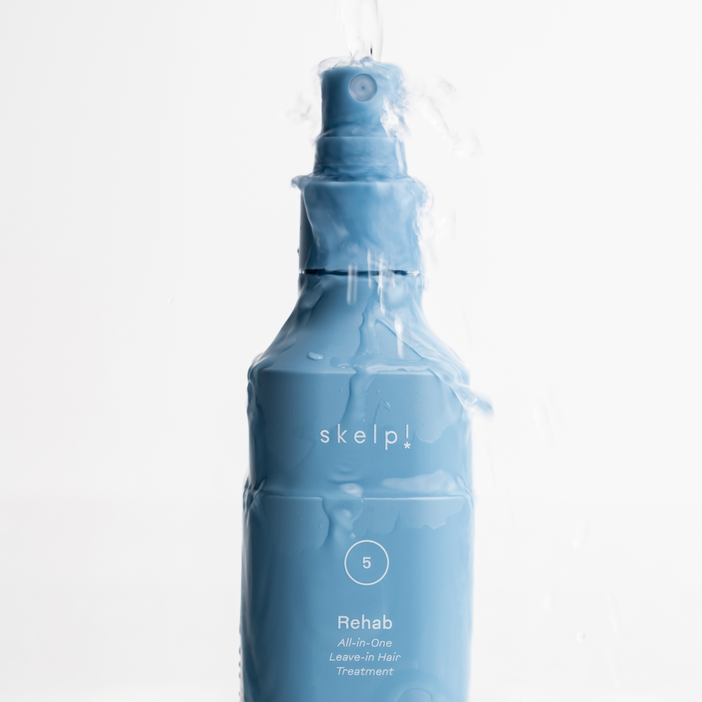 skelp! rehab all in on leave in hair treatment bottle with water pouring over it.