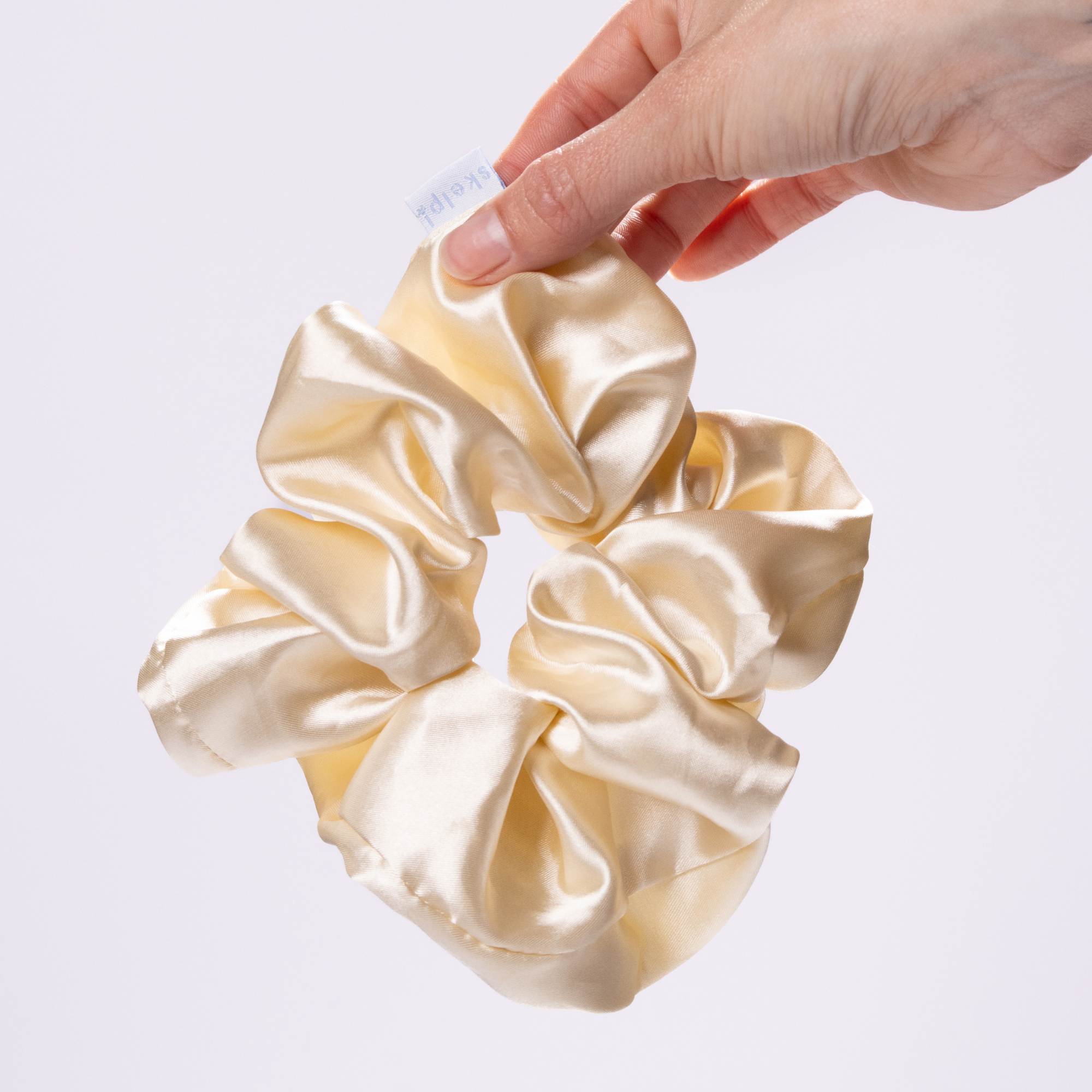 skelp! premium beige satin scrunchie held by a hand on a light gray background