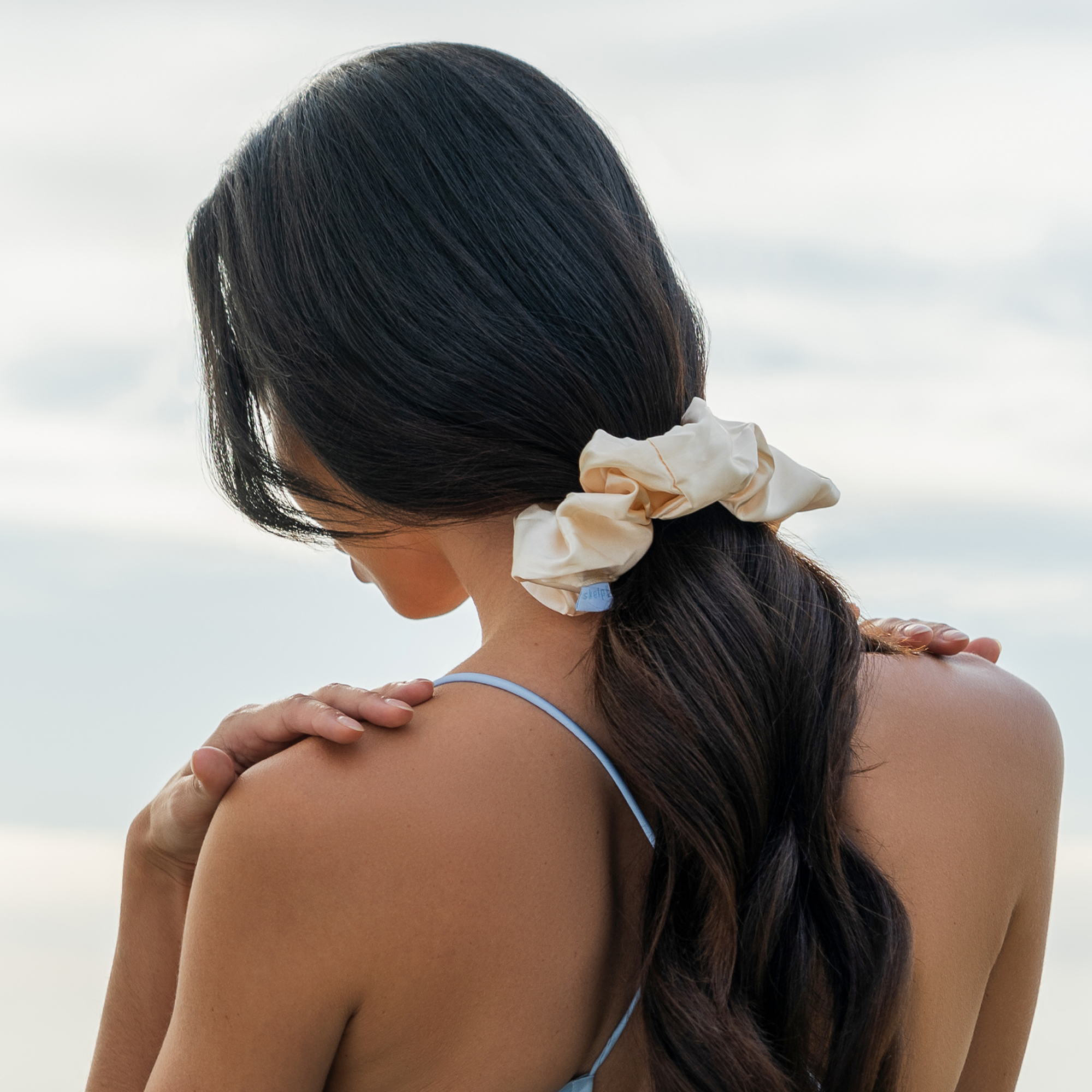 Woman with a skelp silk premium scrunchie in her hair against a cloudy sky background