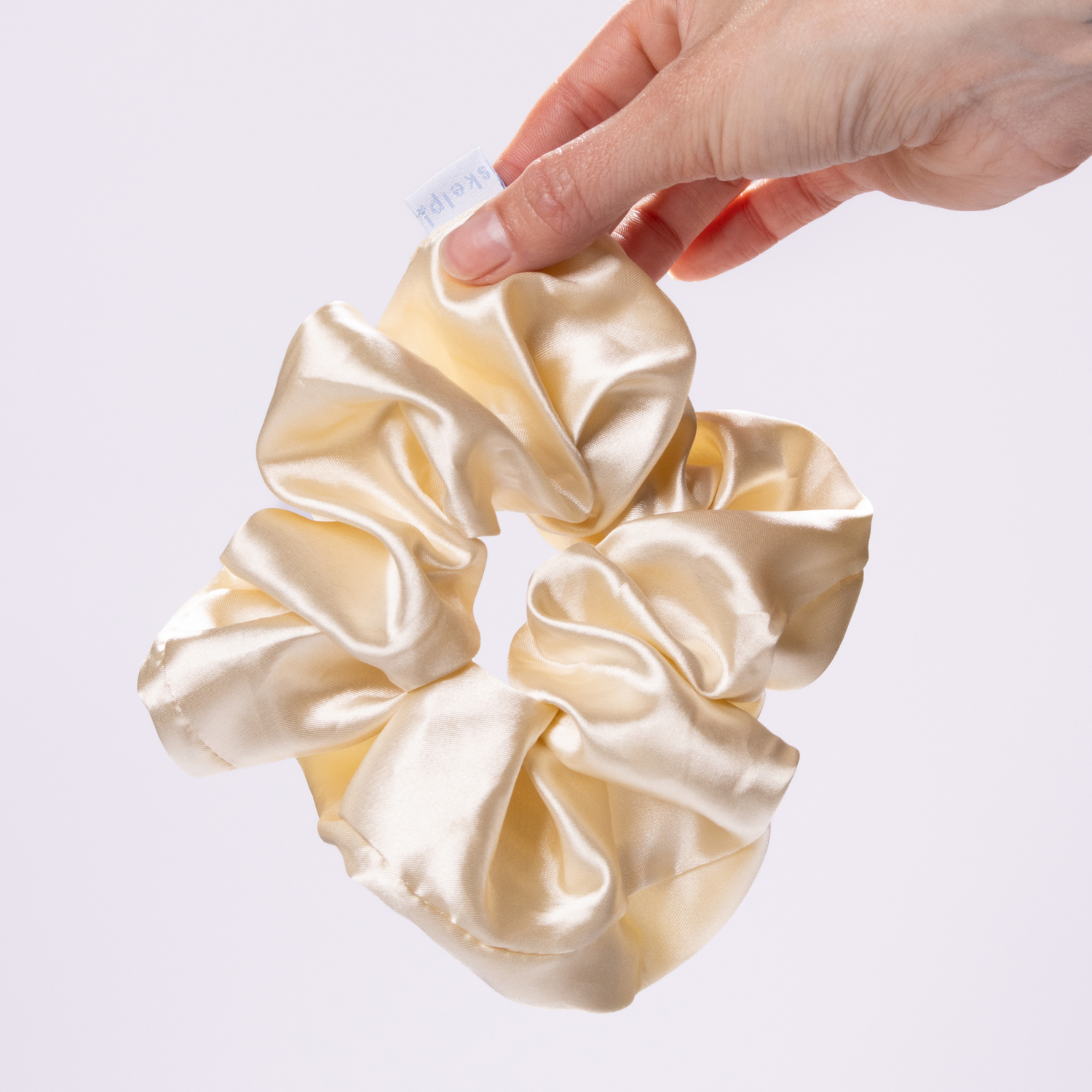 skelp! premium beige satin scrunchie held by a hand on a light gray background