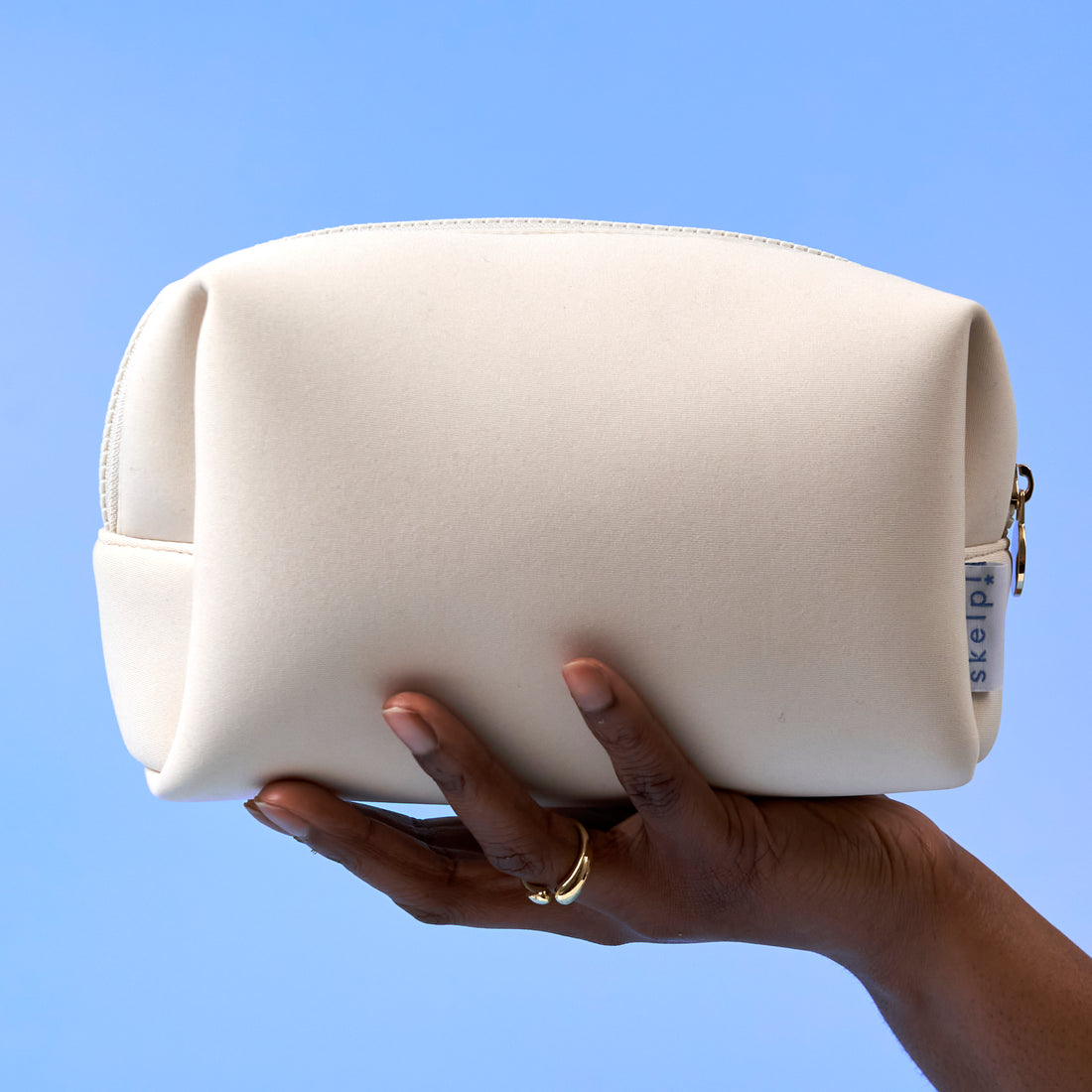 beautiful hand holding premium travel makeup bag in soft cream neoprene fabric for skelp! haircare brand. 