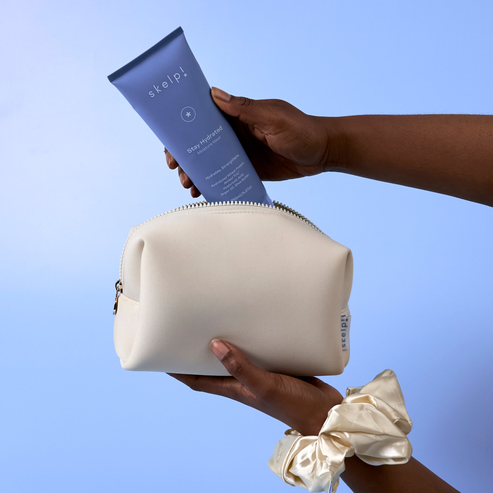 Hand holding a cream cosmetic bag with a purple tube of skelp hair mask and scrunchie on arm